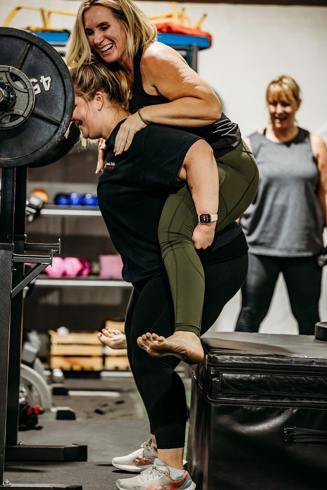 A coach supporting a member through a deadlift, both smiling